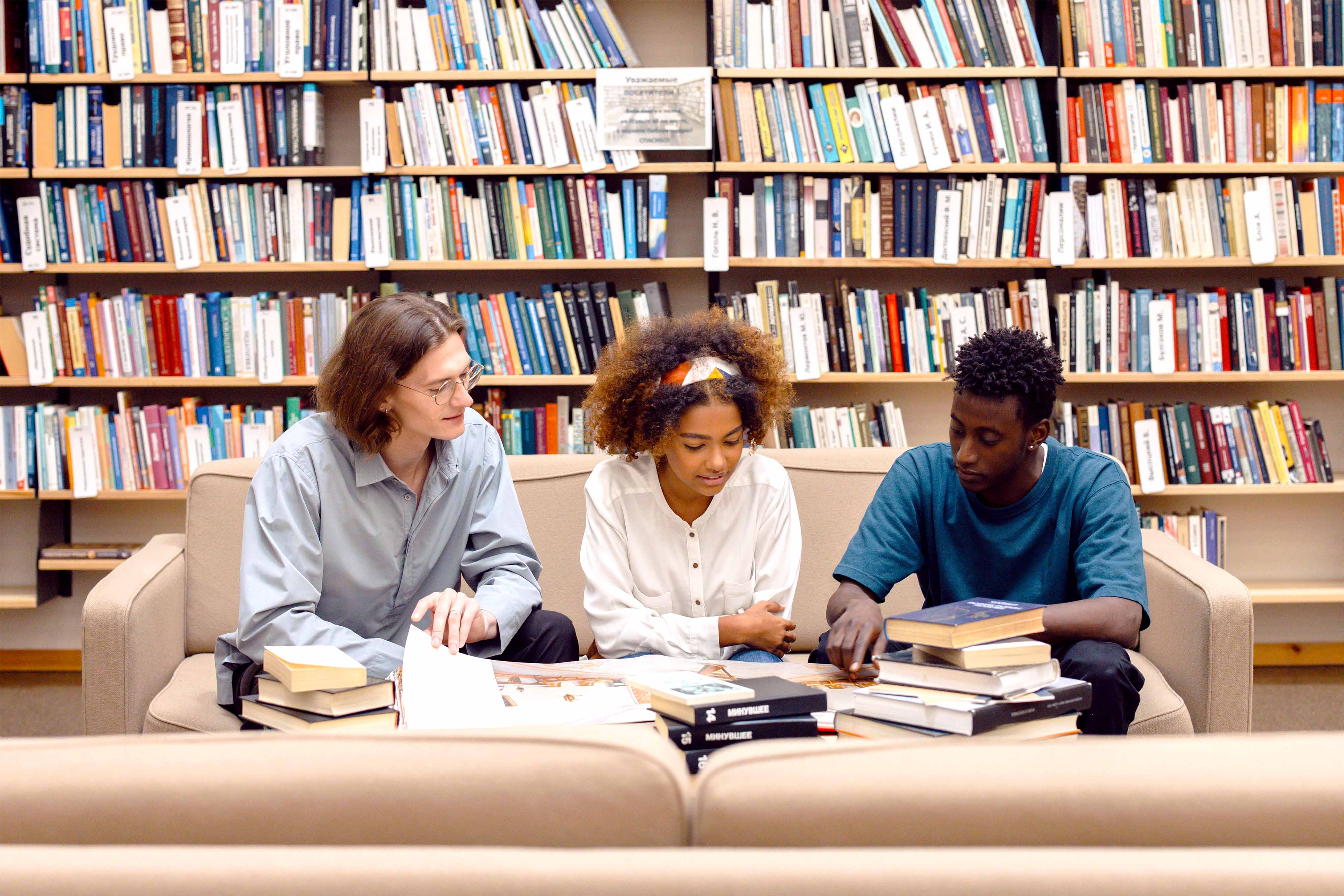 Three people smiling around a laptop in a library